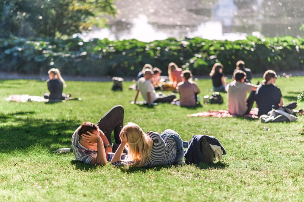 Relaxing summer day in a Danish park, people lounging on the grass, pond water in the background. Concept of hygge.